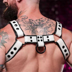 Man with extensive tattoos wearing a white and black leather harness with metal rings, highlighting statement fashion style