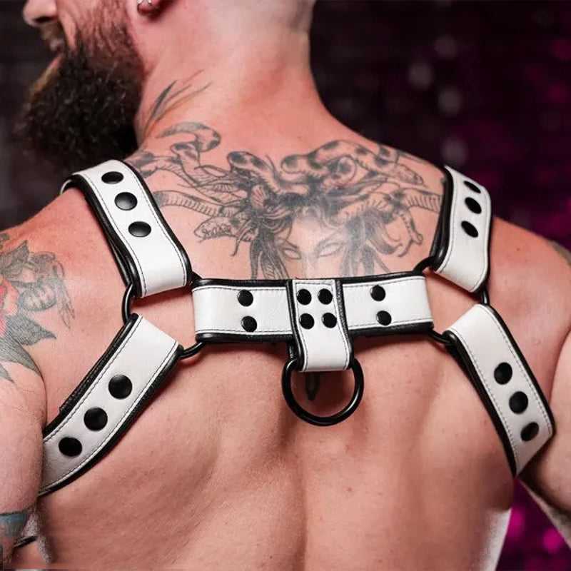 Man with extensive tattoos wearing a white and black leather harness with metal rings, highlighting statement fashion style