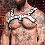 Men's white thickened and black contrasting leather harness with adjustable straps and metal rings, worn over tattoos on a muscular chest