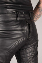 Close-up of black leather pants with padded design, zipper closure, and belt loops, highlighting the smooth leather material and stitching details.