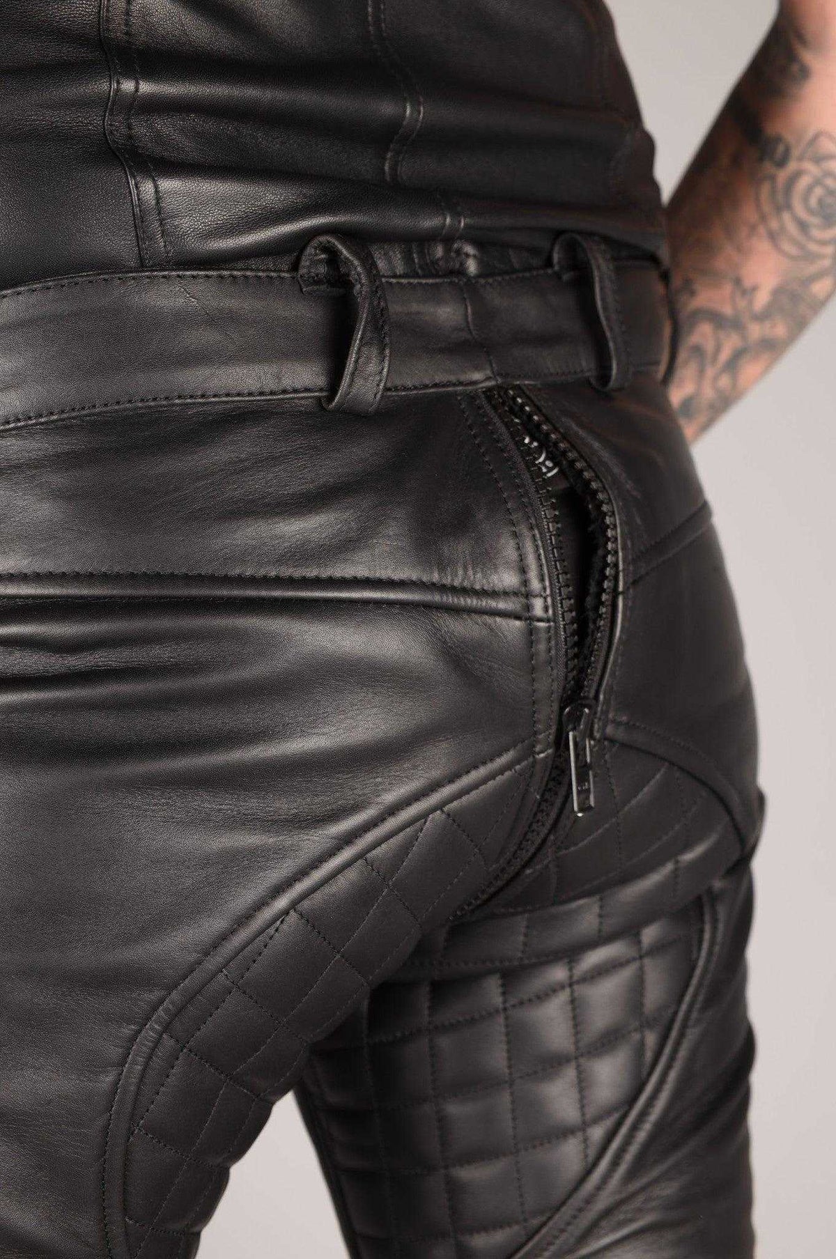 Close-up of black leather pants with padded design, zipper closure, and belt loops, highlighting the smooth leather material and stitching details.