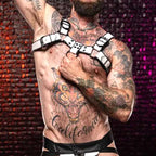Close-up of a tattooed man wearing a white and black leather harness with adjustable straps, showcasing bold fashion accessories